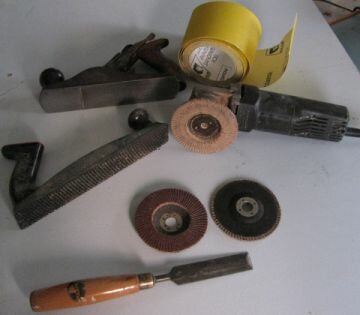 Some tools including an angle grinder with flapper disk, 2 flapper disks, chisel, surform and Stanley planes and a roll of sandpaper